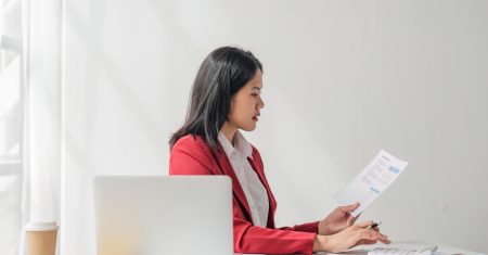 Businesswoman using a calculator to check company finances and earnings and budget. Business woman calculating monthly expenses, managing budget, papers, loan documents, invoices.